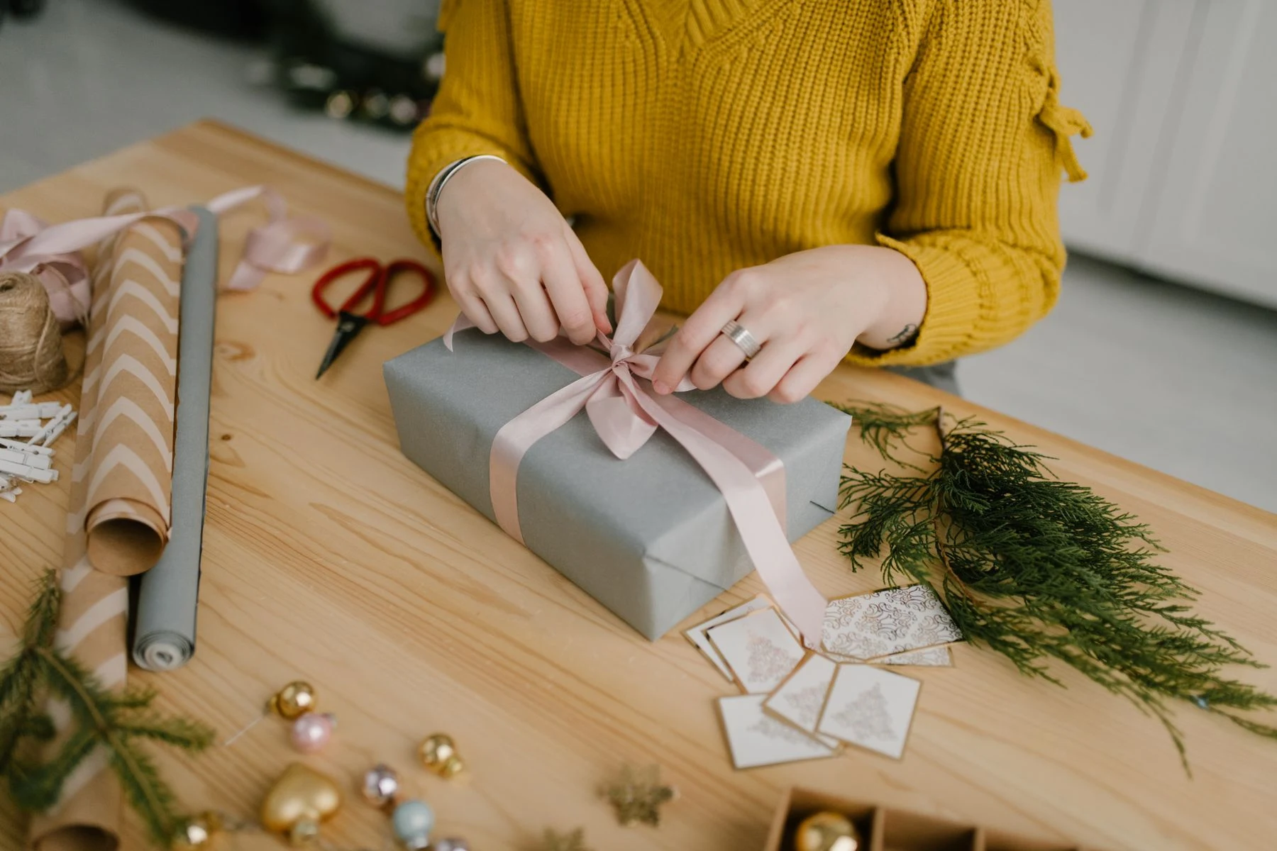 Hände binden eine rosa Schleife um ein Geschenk